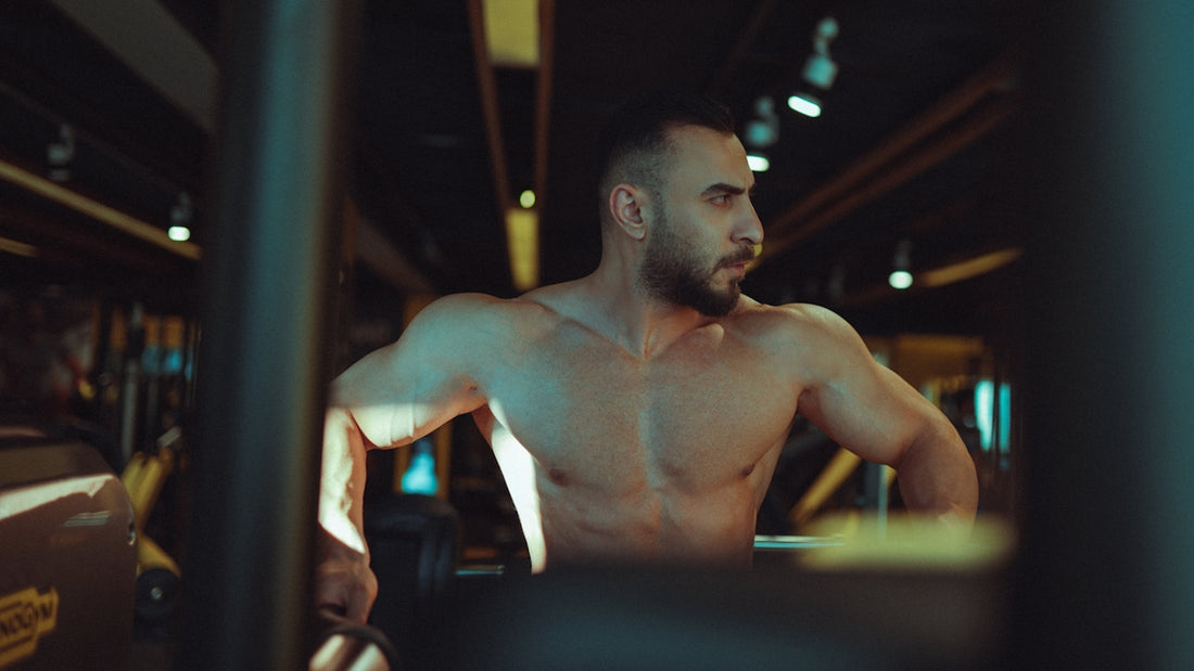 a shirtless man in a gym holding a barbell